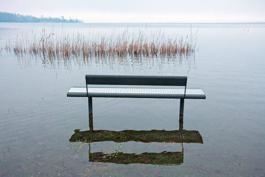 One benche in the park, by the lake, are submerged by water on a winter day.