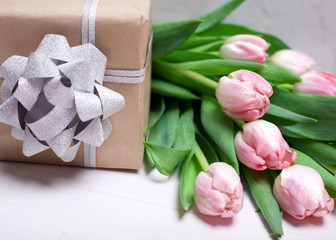 Pink tulips on a white wooden background with a gift and a silver bow