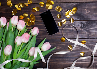 bouquet of tulips on a dark wooden background with golden confetti and mobile phone