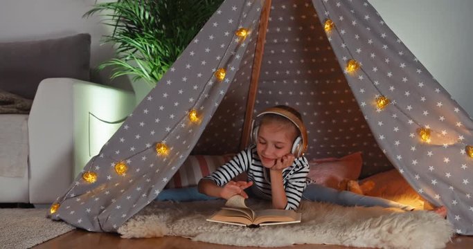 Girl reading book and listening music in wigwam