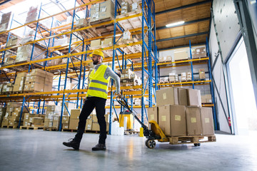 Male warehouse worker pulling a pallet truck. - Powered by Adobe