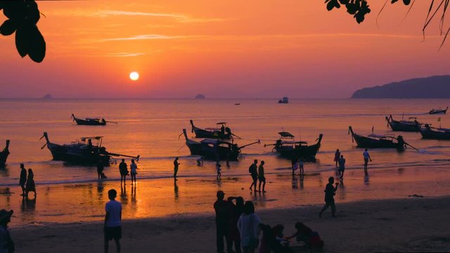 Silhouettes of people and long-tail boats on the Thai beach at sunset