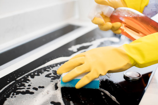 Close Up Of Woman Wearing Rubber Gloves Cleaning Kitchen Hob