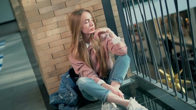 Young stylish girl sitting on the floor wears jeans and white choes, indoor slowmotion