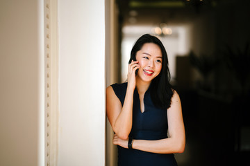 Portrait of a professional businesswoman standing in the middle of a corridor and talking on the phone. She appears to be smiling. 