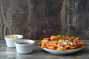 Mexican nachos with beef, guacamole, cheese sauce, peppers, tomato and onion in plate on wooden table