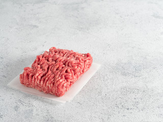 Fresh raw minced beef on backing paper over light gray cement background with copy space.