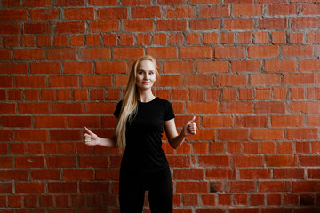 Portrait of beautiful blonde  woman in black sportswear standing against the background of a red brick wall after fitness workout.Fites concept. The girl poses, the place for copy spase nearby