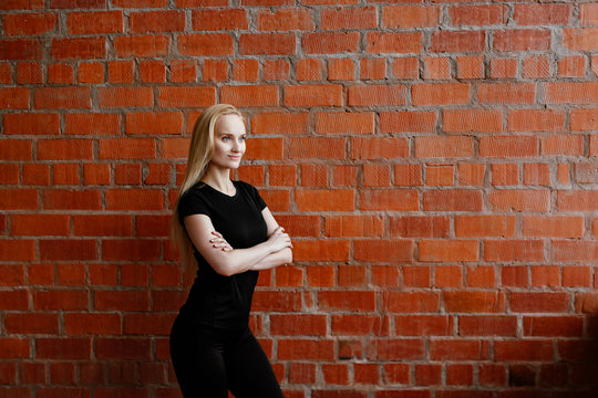 Portrait of beautiful blonde  woman in black sportswear standing against the background of a red brick wall after fitness workout.Fites concept. The girl poses, the place for copy spase nearby