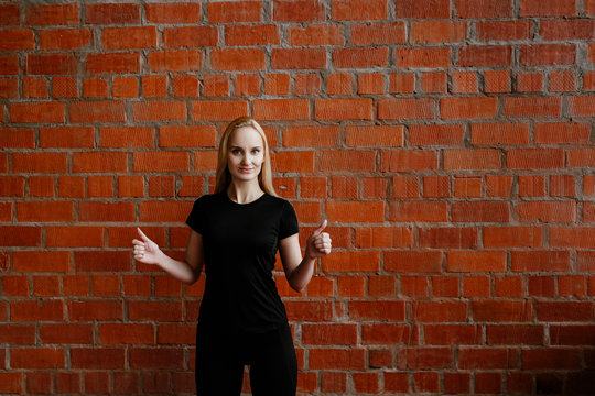 Portrait of beautiful blonde  woman in black sportswear standing against the background of a red brick wall after fitness workout.Fites concept. The girl poses, the place for copy spase nearby
