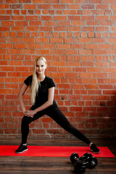 Portrait of beautiful blonde  woman in black sportswear standing against the background of a red brick wall after fitness workout.Fites concept. The girl does warm-up before a fitness training.