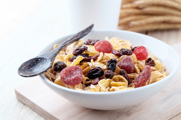 cornflakes and dry berry fruits in a white bowl on a wooden background.
