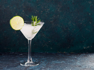 Glass of Martini coctail with fresh rosemary and lime on blue background.