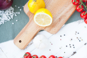 Diet, Healthy Food Cooking, Vegetarian Concept. Set of indredients: fresh cherry tomatoes, lemon on a cutting board, red onion, salt grains and black pepper corns on white wooden table