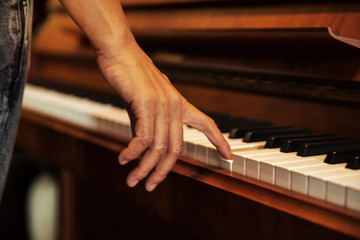 Obraz premium The human hand is pressing on piano key,vintage warm light tone,classic old film design,blurry light around.