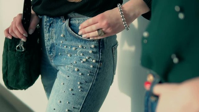 Two sylish young women wears jeans denim posing before white wall, indoor slowmotion
