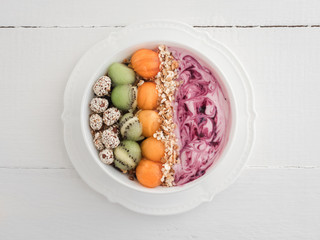 Healthy and delicious food - berry smoothie and muesli with nuts and sesame seeds, pieces of kiwi and persimmon in a white plate on a stylish table, close-up, top view