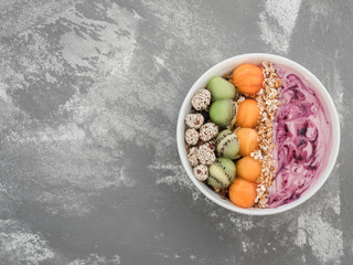 Healthy and delicious food - berry smoothie and muesli with nuts and sesame seeds, pieces of kiwi and persimmon in a white plate on a stylish gray table, close-up, top view