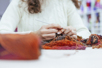 close up of the hands of a working woman while knitting a scarf