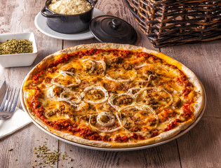 Pizza Bolognese served with onions, oregano and cheese on a rustic wooden table.
