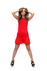 Fototapeta premium Sexy girl in red dress in stockings and in high heels shoes is standing with her legs wide apart and is holding her head by her hands isolated on white background.