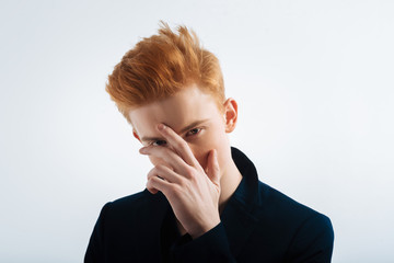 Dark-eyed. Attractive serious red-headed young man wearing a black jacket and touching his forehead...