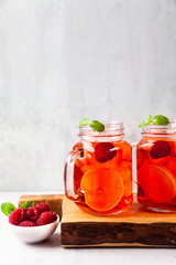 summer refreshing drink with ice and fresh ripe berries. raspberries and blackberries with citrus on a stone background table in glass jars with handles on a wooden serving board