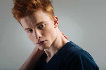 Thoughts. Good-looking upset red-haired young man looking sadly and thinking and touching his neck