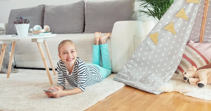 Girl using cell phone. Child lying on the carpet in the living room