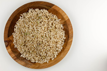 Healthy, raw brown rice in the wooden bowl on the white background