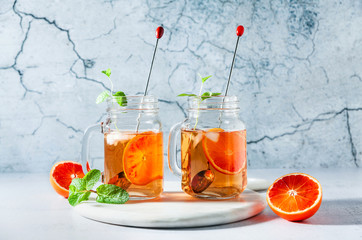 Traditional iced tea with orange and mint and ice in mason jars . refreshing summer drink on white marble board with orange and mint and ice in mason jars . refreshing summer drink