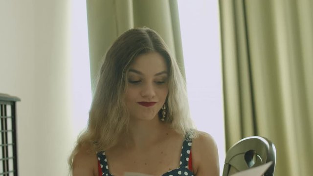 Blonde with wavy hair flips through the menu, then calls and makes an order in the hotel room - Powered by Adobe