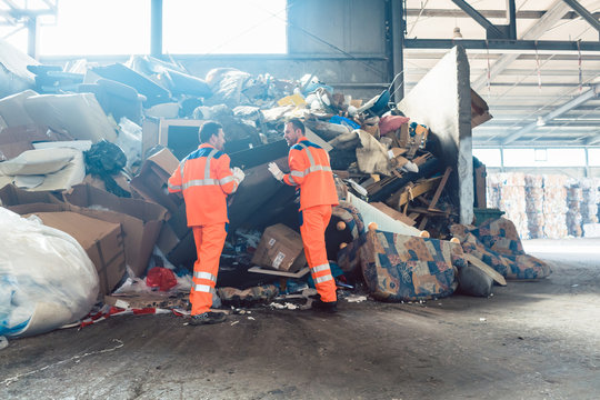Two workers in recycling facility standing in front of a garbage heap to be sorted