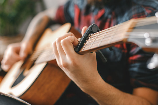 Young guitarist hipster at home with guitar holding capo