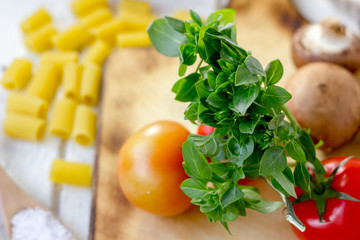 Green basil leaves on kitchen board with vegetables.
