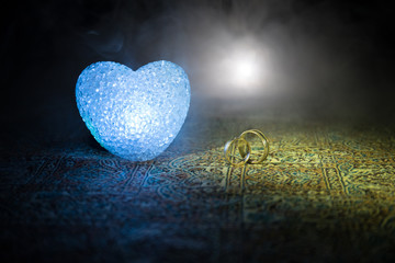 Marriage proposal with gold wedding rings and heart. Valentine concept. Dark toned foggy background.