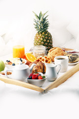 breakfast in bed with fruits and pastries on a tray -waffles, croissants, coffe and juice