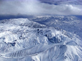 Hindu Kush Mountains - snow-covered peaks of mountains with clouds in the background seen from the plane