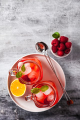summer refreshing drink with ice and fresh ripe berries. raspberries and blackberries with citrus on a stone background table in glass jars with handles