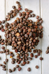 Heap of fresh and ripe pine nuts over white wooden table.