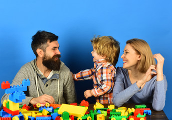 Family with happy faces communicate near colored construction blocks.