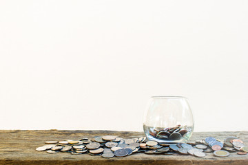 Many coins in clear glass on wooden table on white background with copy space.