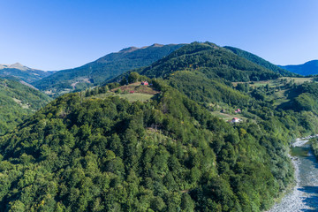 Fototapeta premium The house on a mountain of red color is surrounded by green trees. aerial view.
