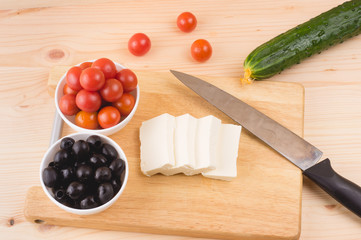 Greek salad with vegetables, feta cheese, black olives in process. Wooden background . Top view