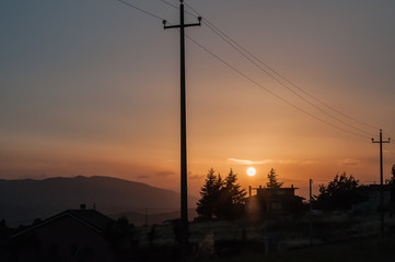 palo della luce in primo piano e sagome di abati controluce, sullo sfondo montagne durante un tramonto