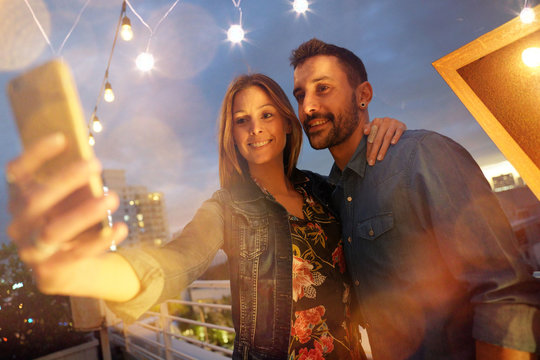 Young couple on rooftop at night taking selfie picture