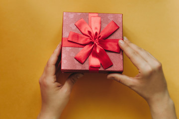 The girl has received a gift in a beautiful red box with a ribbon and is going to open it.