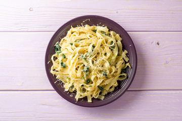 Tagliatelle pasta with spinach, garlic and Parmesan cheese on purple wooden background.