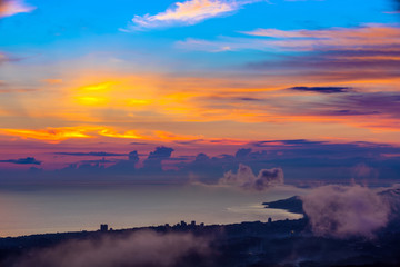 Silhouette of the Black Sea coast under cumulus clouds in the bright orange colorful sky of the setting sun. Panorama of the coast from the observation tower on Mount Akhun.