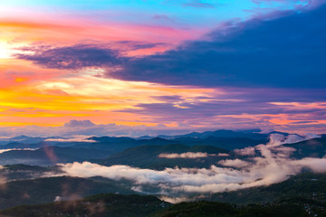 The mountain valley in the evening in the fog is lit by the sunset under beautiful colorful clouds of yellow blue violet red. Panorama of the coast from the observation tower on Mount Akhun.
